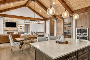 A spacious kitchen with a central island, wooden beams, and pendant lighting. - Love & Sunsets at Eagles Nest - hot tub, expansive mountain view, outdoor fireplace (Banner Elk)