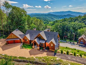 A cabin with a gravel driveway, surrounded by lush greenery and mountains in the background. - Love & Sunsets at Eagles Nest - hot tub, expansive mountain view, outdoor fireplace (Banner Elk)