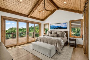 A bedroom with a large bed, a view of the outdoors, and a ceiling fan. - Love & Sunsets at Eagles Nest - hot tub, expansive mountain view, outdoor fireplace (Banner Elk)