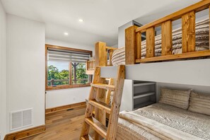 A bunk bed with a wooden ladder, a window with blinds, and a bed with patterned bedding. - Love & Sunsets at Eagles Nest - hot tub, expansive mountain view, outdoor fireplace (Banner Elk)