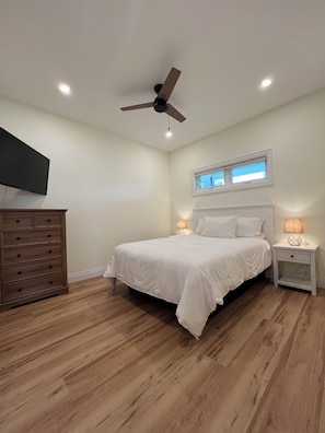 A bedroom with a bed, a nightstand, a dresser, a ceiling fan, and a window.