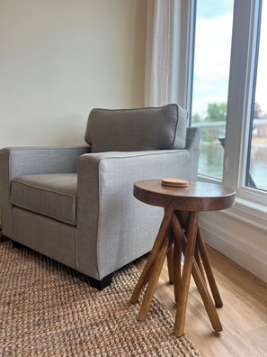 A grey armchair with wooden legs, a woven rug, and a small wooden table.