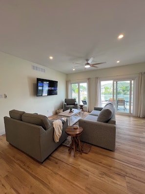 A living room with a flat-screen TV, two sofas, a coffee table, and a ceiling fan.