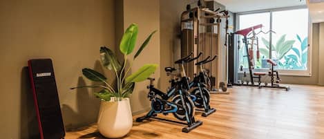 Une salle de sport équipée de vélos d’exercice, d’une machine de musculation et d’une grande fenêtre donnant sur un paysage verdoyant.