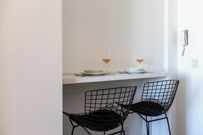 A small dining area with two black wire chairs, a white table, and two glasses of wine. - Modern Studio with Pool, Gym, and Private Grill—Palermo (Buenos Aires)