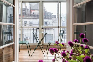 Ein Balkon mit Glastisch und Stühlen, mit Blick auf eine Stadtlandschaft.