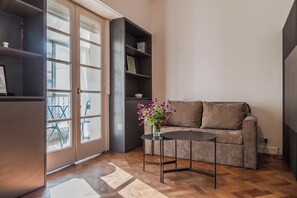 Ein Wohnzimmer mit einer Couch, einem kleinen Tisch mit Blumenvase und einem Bücherregal.
