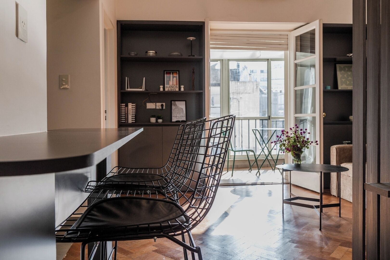 Una cocina moderna con comedor, que incluye una silla metálica, una mesita y una estantería con objetos decorativos.