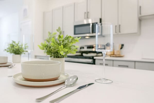 A modern kitchen with white cabinets, a microwave, and a dining table with a bowl, spoon, and glass. - Peaceful 1BR Stay - Pool & Gym Access (Sherman)