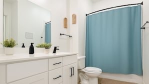 Un baño moderno con tocador blanco, pomos negros, inodoro blanco y cortina de ducha azul.