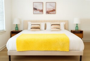A neatly made bed with a yellow blanket, two bedside tables with lamps, and two framed pictures on the wall. - Peaceful 1BR Stay - Pool & Gym Access  (Sherman)