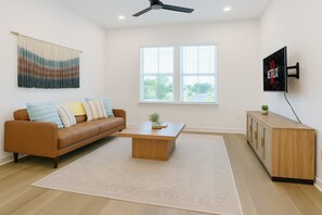 A modern living room with a brown leather sofa, a wooden coffee table, and a TV mounted on the wall. - Peaceful 1BR Stay - Pool & Gym Access  (Sherman)