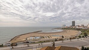 Paesaggio costiero con spiaggia, passeggiata e edifici moderni.