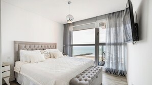 Una camera da letto con un letto grande, una panca, un comodino, una televisione e vista mare.