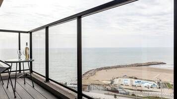 A balcony with a view of the sea, a table with a bottle and glasses, and a chair.