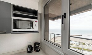 Une petite cuisine équipée d’un four à micro-ondes encastré, d’une machine à café et offrant une vue sur la plage grâce à une grande fenêtre.