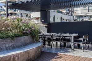 An outdoor seating area with a modern design, featuring a concrete planter with plants and a wooden deck. - Premium Studio | Pool, Gym, and Coworking Space (Buenos Aires)