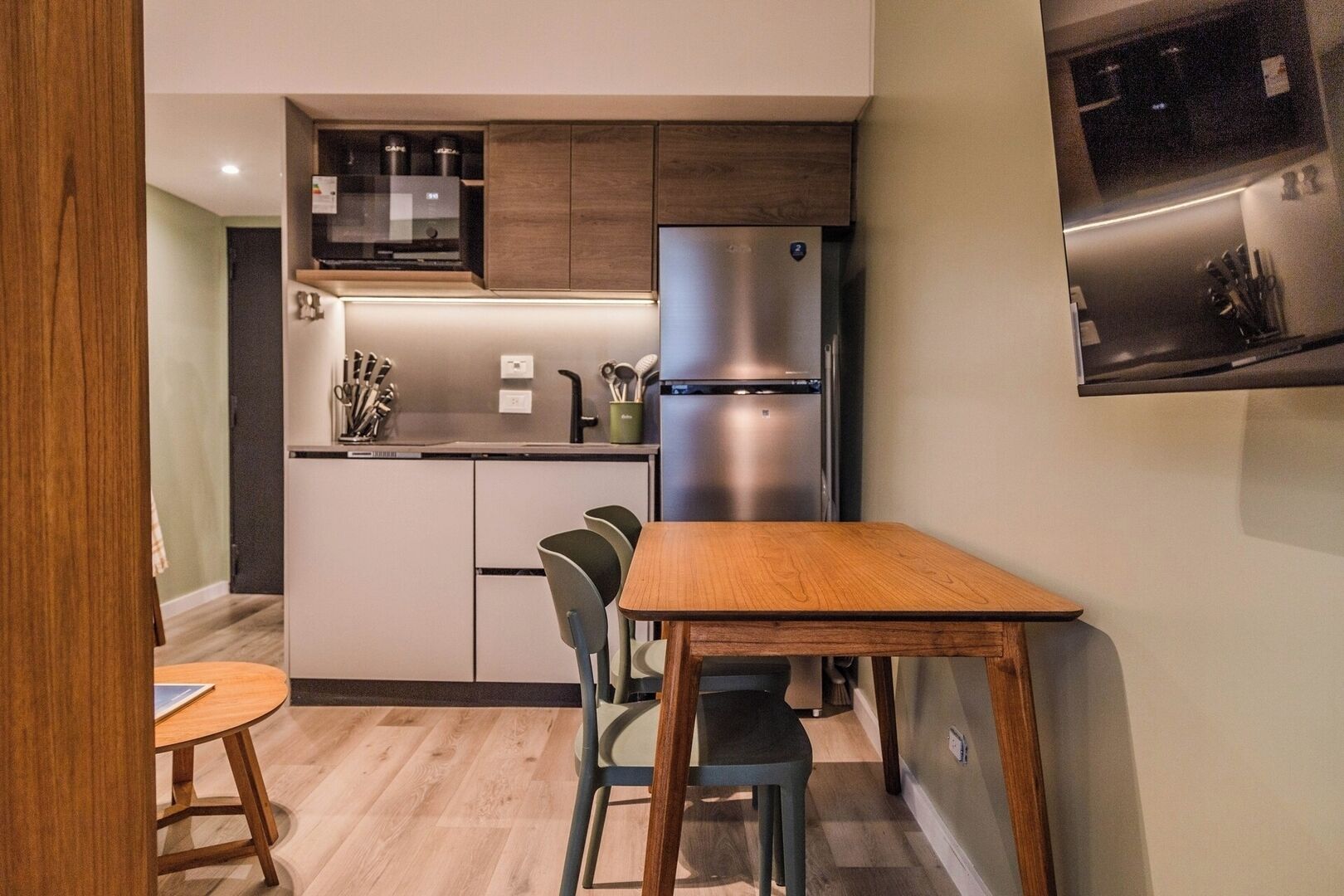 A compact kitchen with a refrigerator, microwave, and cabinets. There is a dining table with chairs.