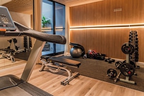 A gym with cardio equipment, weightlifting stations, and a wooden floor. - Premium Studio | Pool, Gym, and Coworking Space (Buenos Aires)