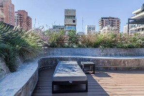 An outdoor seating area with a bench and a table, surrounded by greenery and overlooking a cityscape. - Premium Studio | Pool, Gym, and Coworking Space (Buenos Aires)