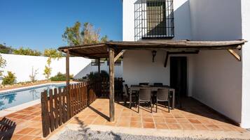 Un patio con piscina, mobiliario exterior y una pérgola.