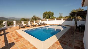 Una piscina rectangular con borde blanco, rodeada por un muro blanco y una cerca de madera.