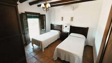 Una habitación con dos camas individuales, techo de madera, una mesita de noche con lámpara y una puerta que da al exterior.
