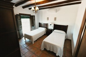 A room with two single beds, a wooden ceiling, a small bedside table with a lamp, and a door leading outside. - Casas de Cantoblaco (Benamargosa)
