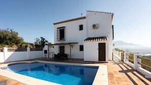 Casa blanca de dos pisos con piscina, mobiliario exterior y vistas a las montañas.
