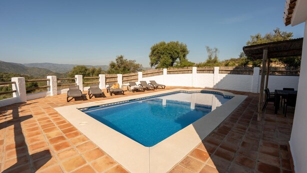 Una piscina rectangular con borde blanco, rodeada por un muro blanco y una cerca de madera.