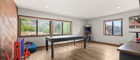 Una habitación con mesa de billar, ventanas con vistas a montañas y una mesa de fútbol.
