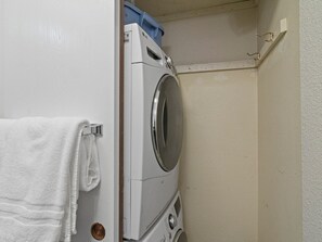 Ein kleiner Waschbereich mit Waschmaschine, Wäscheständer und einem Handtuch an einem Metallhaken.