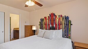 Un dormitorio con cama, ventilador de techo, cómoda y esquíes montados en la pared.