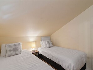 Ein Zimmer mit zwei Einzelbetten, einem Nachttisch mit Lampe und einer schrägen Decke.