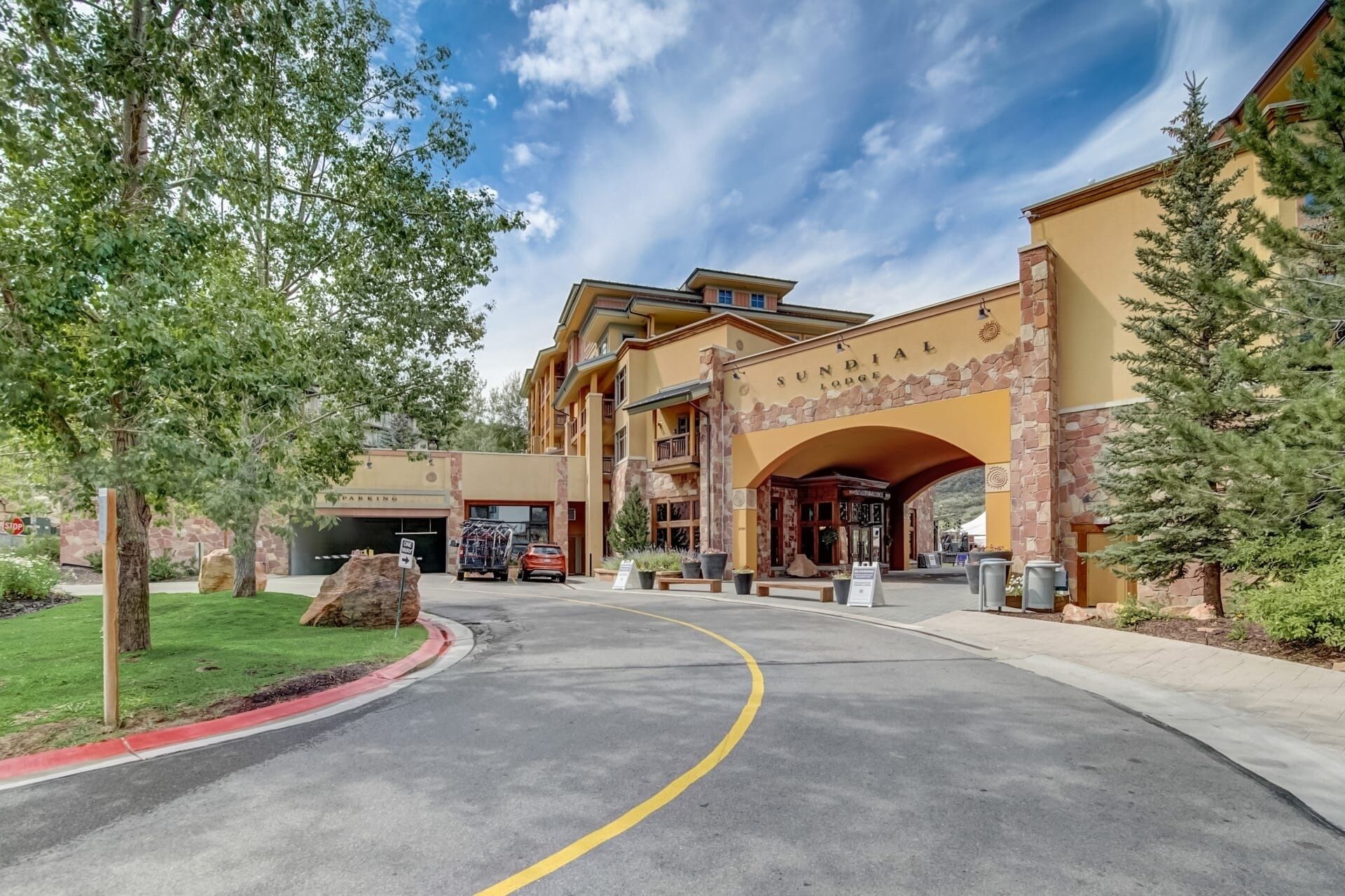A lodge entrance with a stone archway, a parking area, and a clear sky.