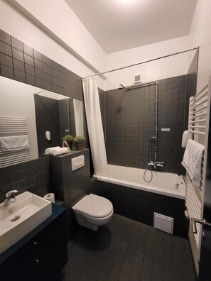 A modern bathroom with a bathtub, toilet, and sink. - Grettisborg Apartments (Reykjavik)