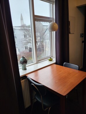 A room with a wooden table, a chair, a window with a view of buildings, and a lamp. - Grettisborg Apartments (Reykjavik)