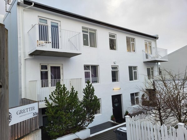 A multi-story residential building with balconies, a sign indicating apartments, and a gated entrance. - Grettisborg Apartments (Reykjavik)