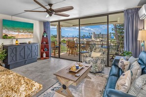 A spacious living area with a large sliding glass door leading to a balcony with a view of the ocean and palm trees. - Kihei Alii Kai B-302 - Ocean Views, Stunning Renovation, King Size Bed, Split AC (Kihei)