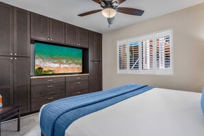 A bedroom with a bed, a television on a cabinet, a ceiling fan, and a window with blinds. - Kihei Alii Kai B-302 - Ocean Views, Stunning Renovation, King Size Bed, Split AC (Kihei)