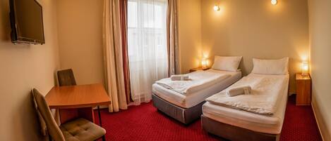 A hotel room with two beds, a desk, a chair, and a window with curtains.