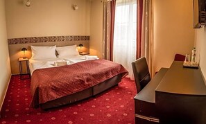 A hotel room with a bed, bedside lamps, a desk, and a chair.
