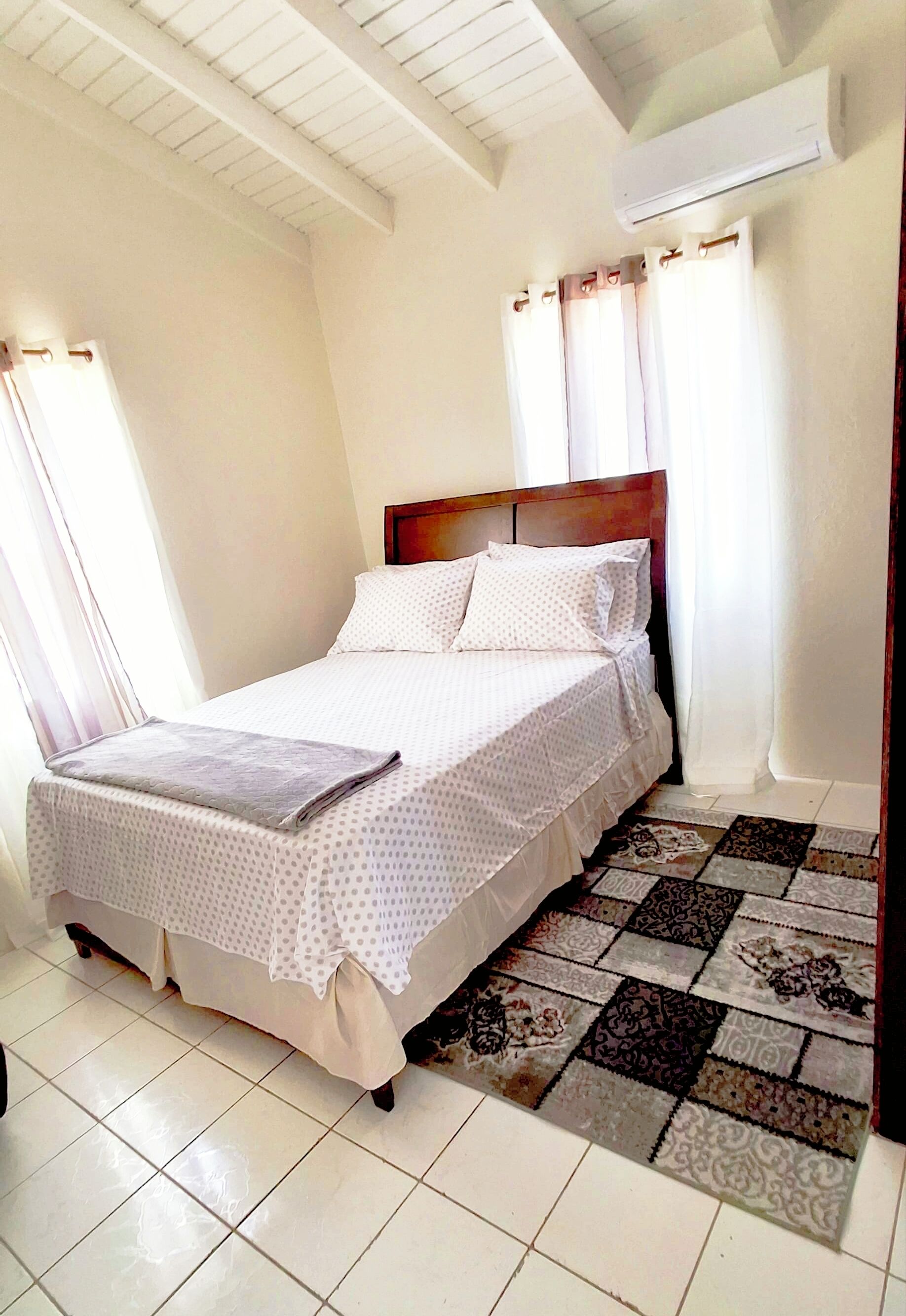 Une chambre à coucher avec un lit, des rideaux, un appareil de climatisation et un tapis à motifs.