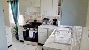 A modern kitchen with white cabinets, a gas stove, an oven, and a sink. - Peaceful 2-bedroom house with AC in Christ Church Parish (Christ Church Nichola Town Parish)
