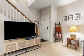 Ein Wohnzimmer mit Flachbildfernseher auf Holzständer, einer Treppe, einer Tür, einem Kleiderständer und einer Lampe.