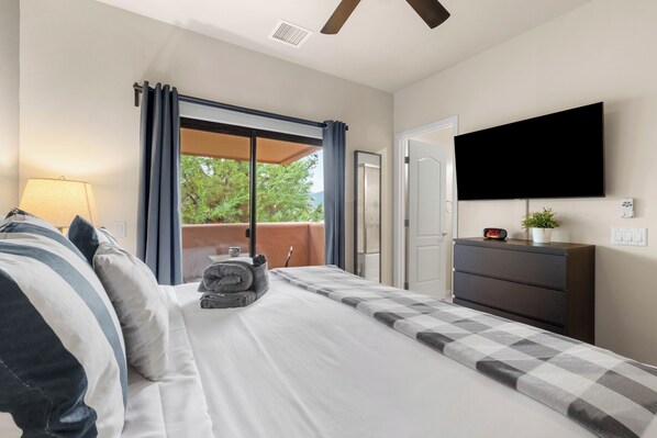 A hotel room with a bed, a TV, a dresser, and a view of greenery outside. - 2BR Sedona retreat with red rock views, hot tub, Wi-Fi, and patio. (Sedona)