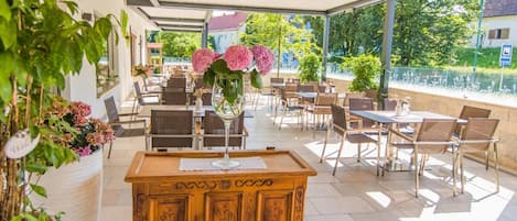 An outdoor patio area with tables and chairs, a wooden bench, and potted plants.