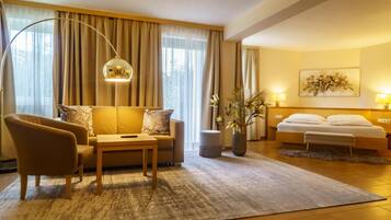 Ein Hotelzimmer mit Sofa, Sessel, Nachttisch, Lampe, Zimmerpflanze und einem Bett mit Kopfteil.