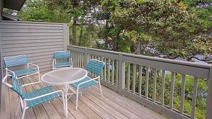 Une terrasse en bois avec une table et quatre chaises, entourée d’une balustrade blanche.