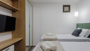 Ett hotellrum med en säng, en tv, en spegel och ett nattduksbord.